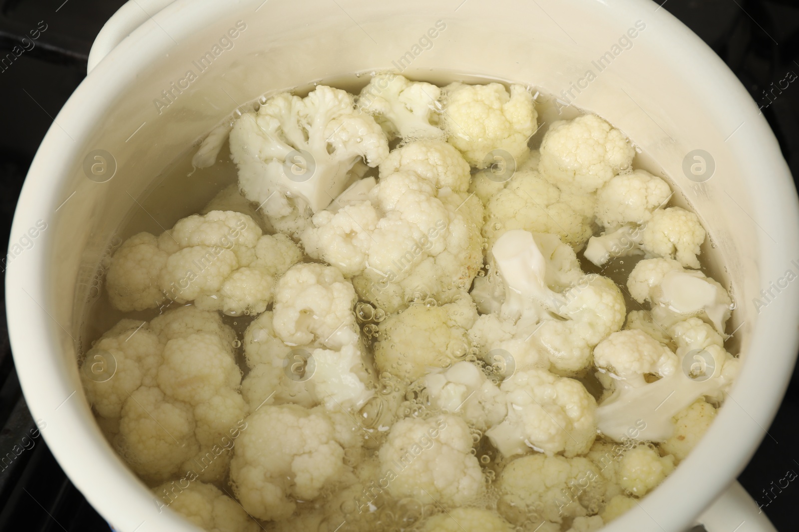 Photo of Cooking cauliflower. Florets in white pot with water on cooktop, closeup