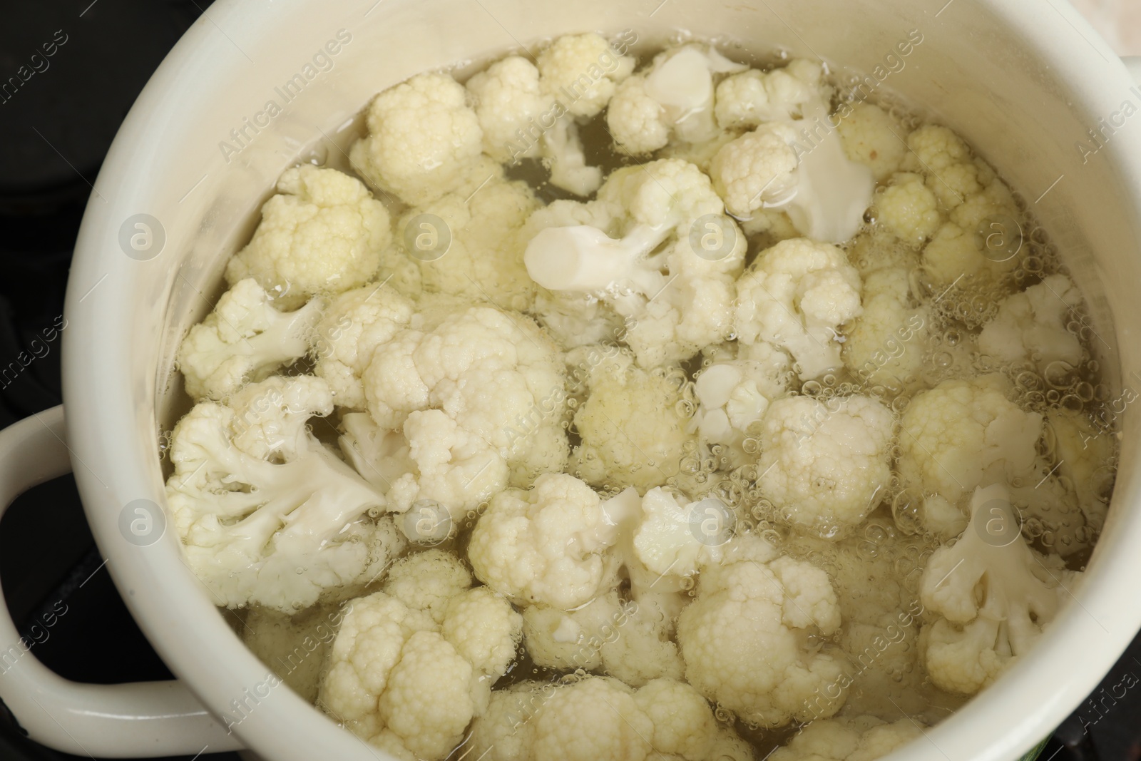 Photo of Cooking cauliflower. Florets in white pot with water on cooktop, closeup