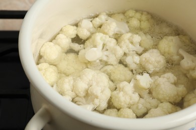 Photo of Cooking cauliflower. Florets in white pot with water on cooktop, closeup