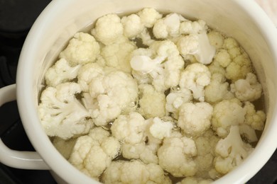 Photo of Cooking cauliflower. Florets in white pot with water on cooktop, closeup