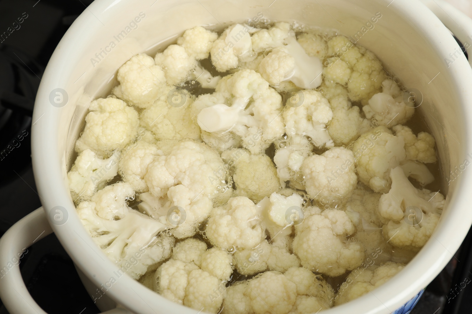 Photo of Cooking cauliflower. Florets in white pot with water on cooktop, closeup