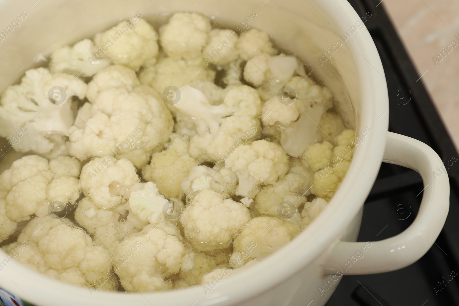 Photo of Cooking cauliflower. Florets in white pot with water on cooktop, closeup