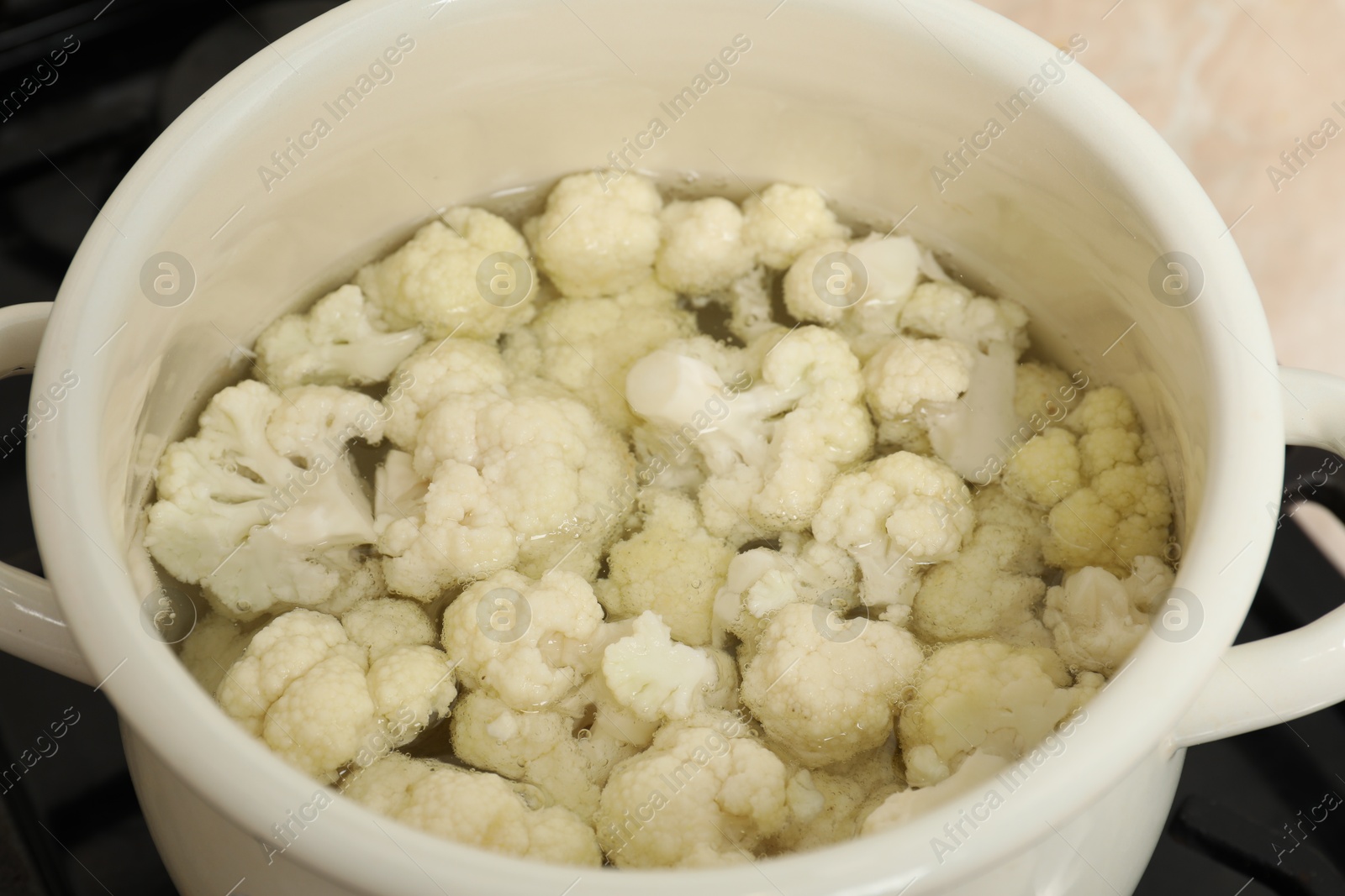 Photo of Cooking cauliflower. Florets in white pot with water on cooktop, closeup