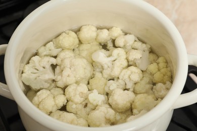 Photo of Cooking cauliflower. Florets in white pot with water on cooktop, closeup