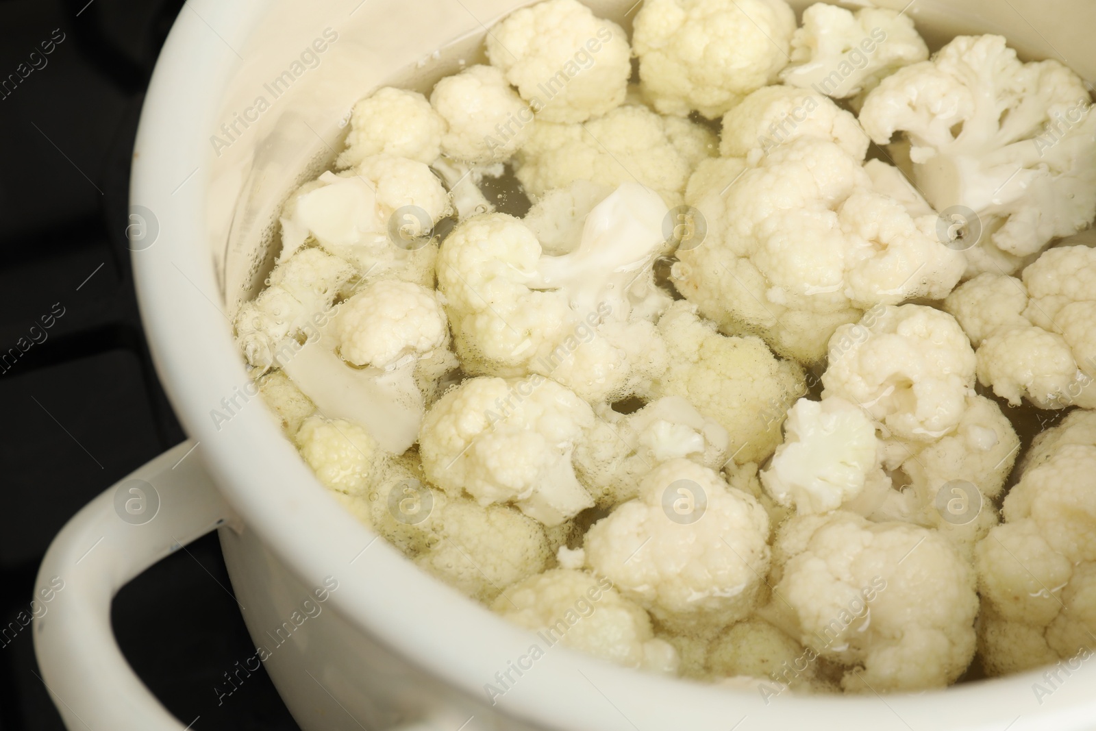 Photo of Cooking cauliflower. Florets in white pot with water on cooktop, closeup