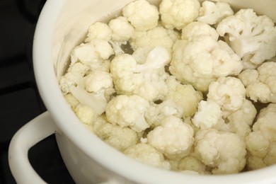 Photo of Cooking cauliflower. Florets in white pot with water on cooktop, closeup