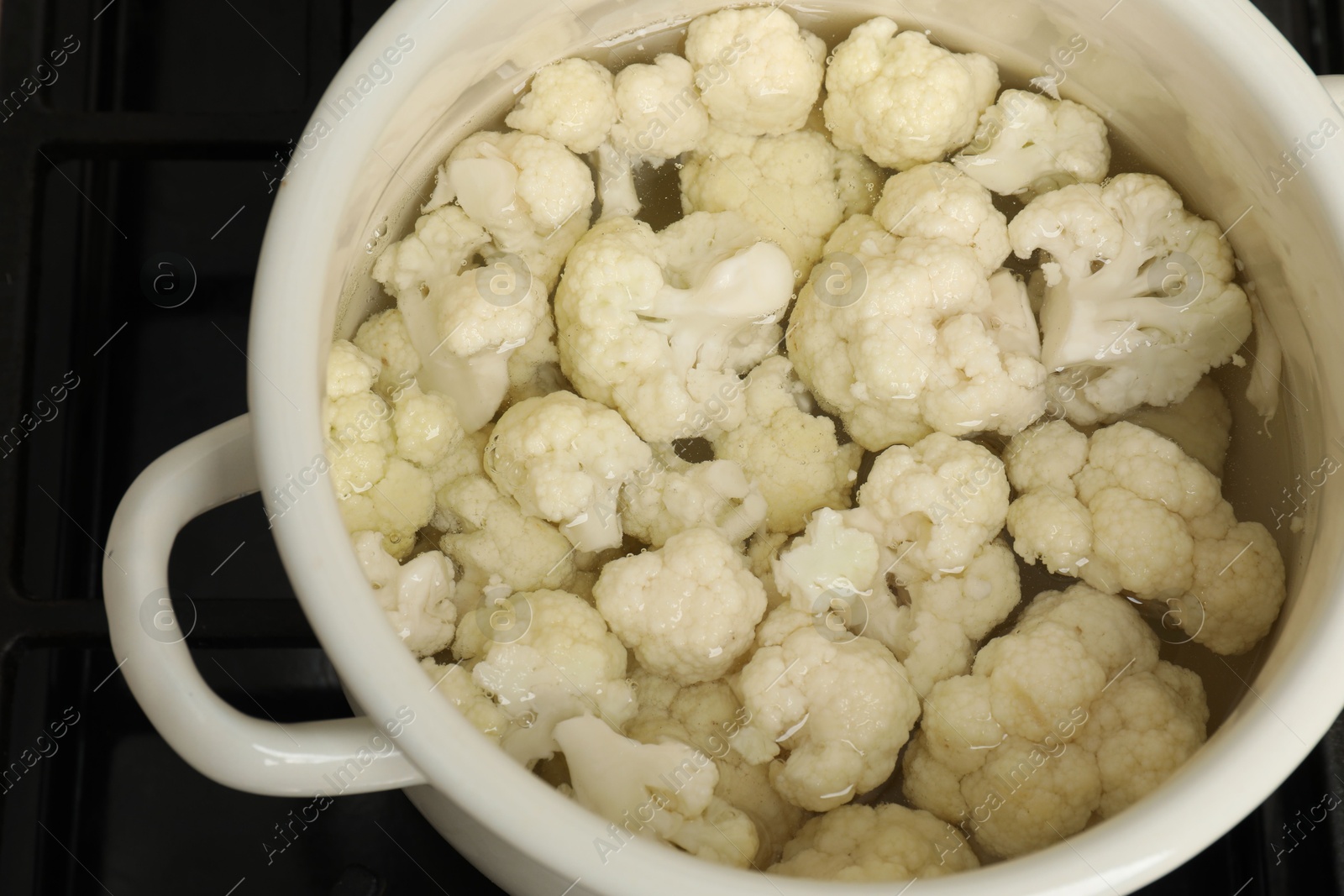 Photo of Cooking cauliflower. Florets in white pot with water on cooktop, closeup