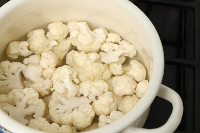 Photo of Cooking cauliflower. Florets in white pot with water on cooktop, closeup