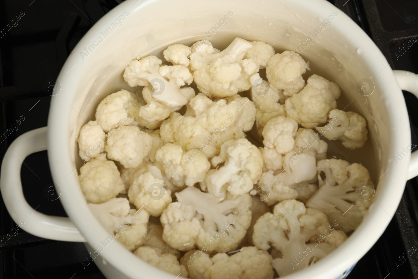 Photo of Cooking cauliflower. Florets in white pot with water on cooktop, closeup