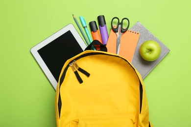 Photo of Backpack, different school stationery and apple on light green background, flat lay