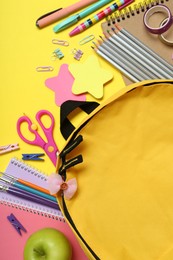 School backpack and stationery on yellow background, flat lay