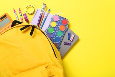 Photo of School backpack and stationery on yellow background, flat lay. Space for text