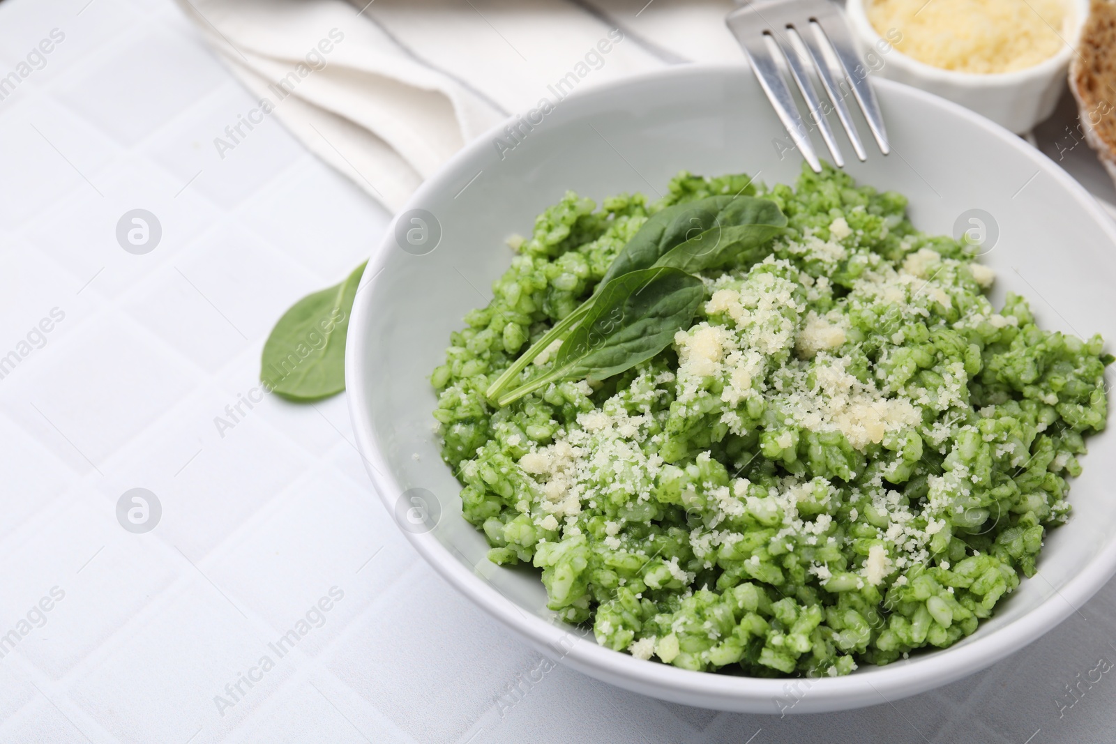 Photo of Delicious spinach risotto with parmesan cheese served on white tiled table, closeup. Space for text