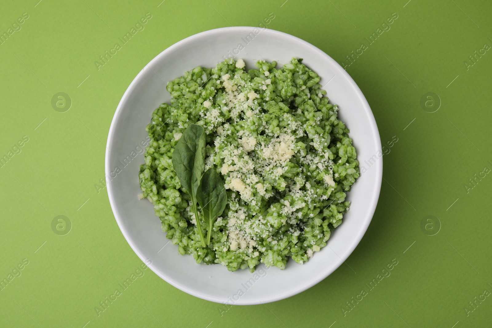 Photo of Delicious spinach risotto with parmesan cheese on light green background, top view