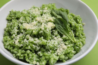 Photo of Delicious spinach risotto with parmesan cheese on light green background, closeup