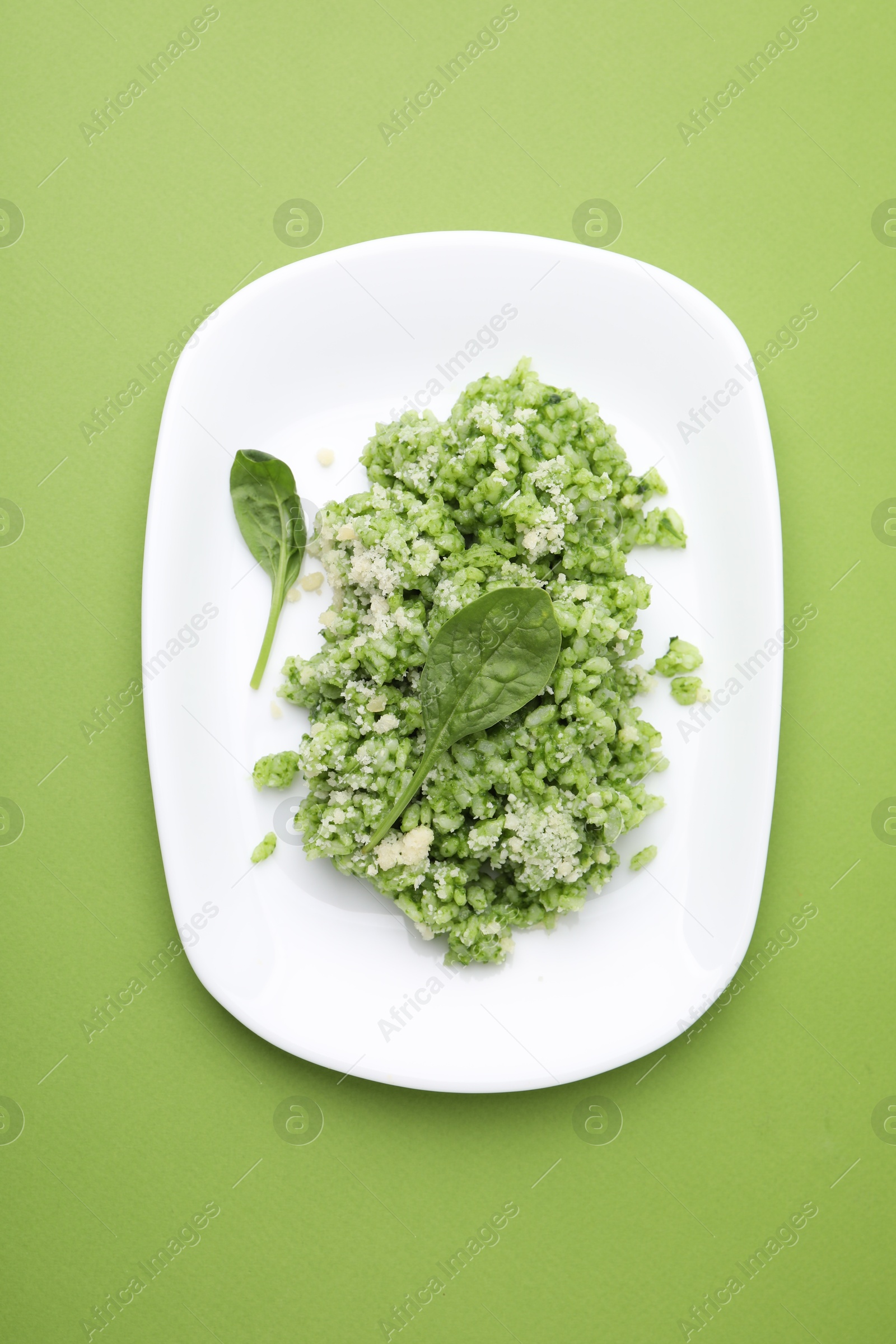 Photo of Delicious spinach risotto with parmesan cheese on light green background, top view