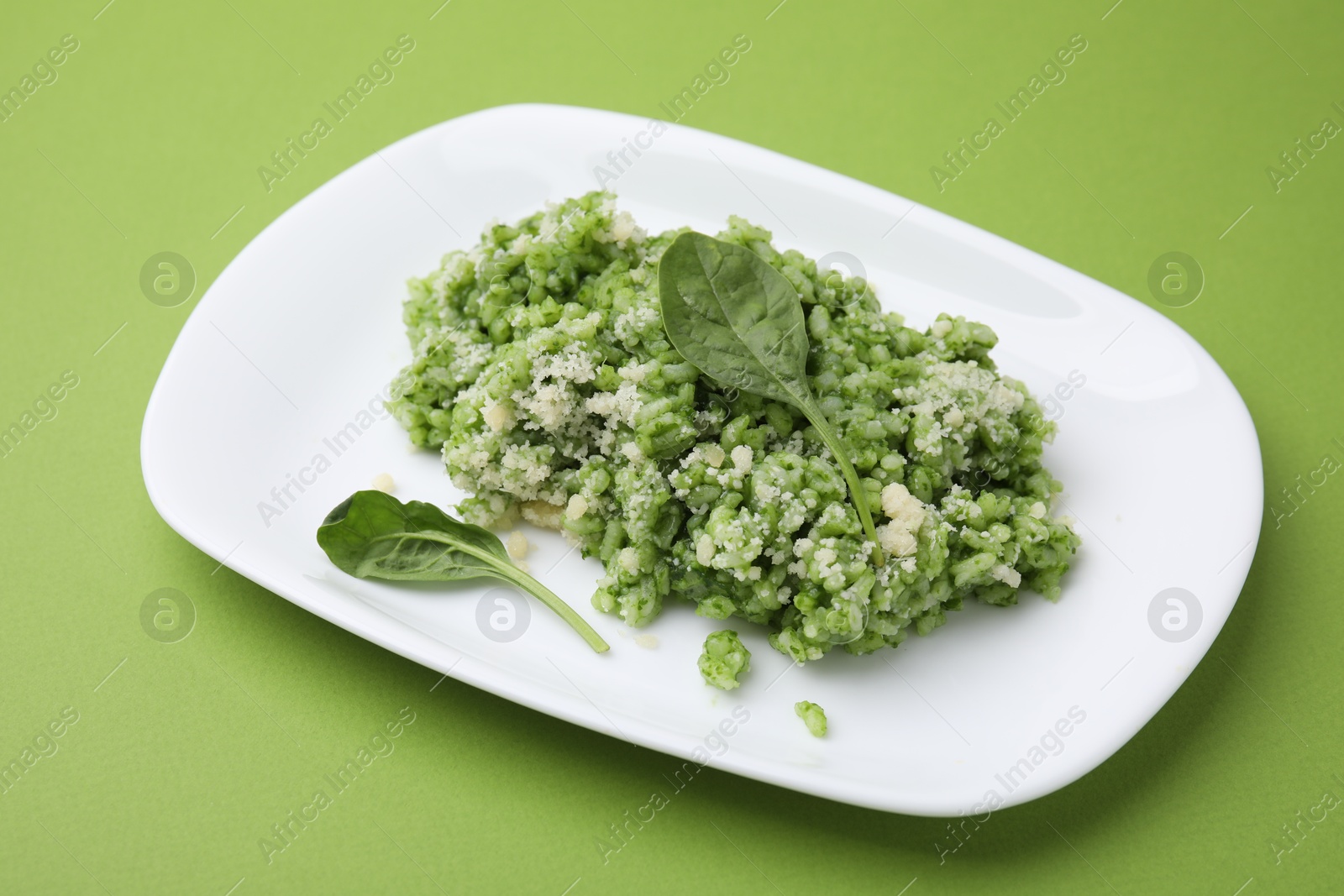 Photo of Delicious spinach risotto with parmesan cheese on light green background