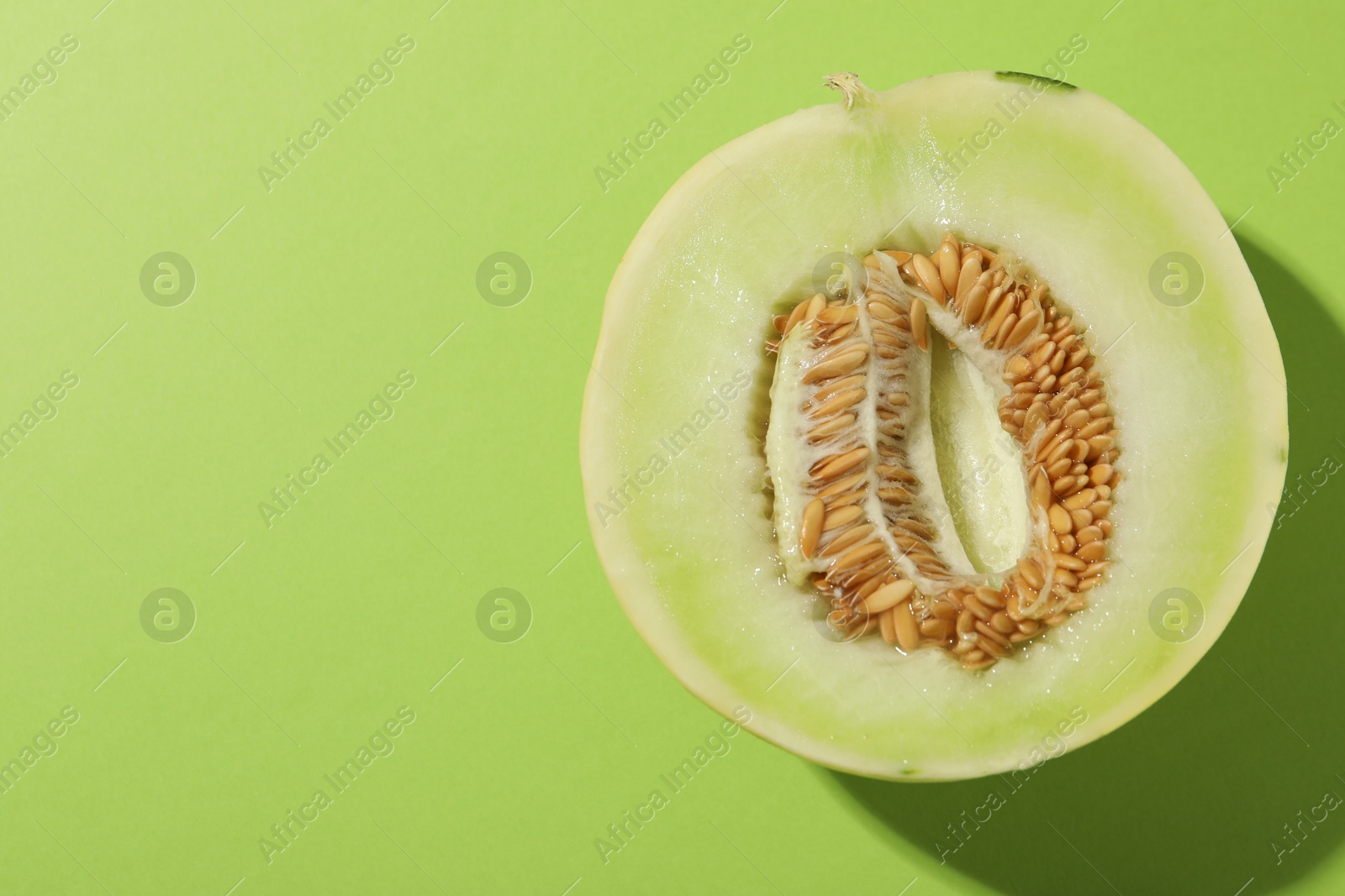 Photo of Half of fresh ripe honeydew melon on green background, top view. Space for text