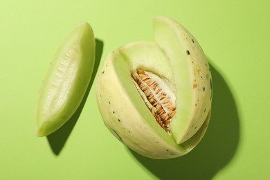 Photo of Cut fresh ripe honeydew melon on green background, top view