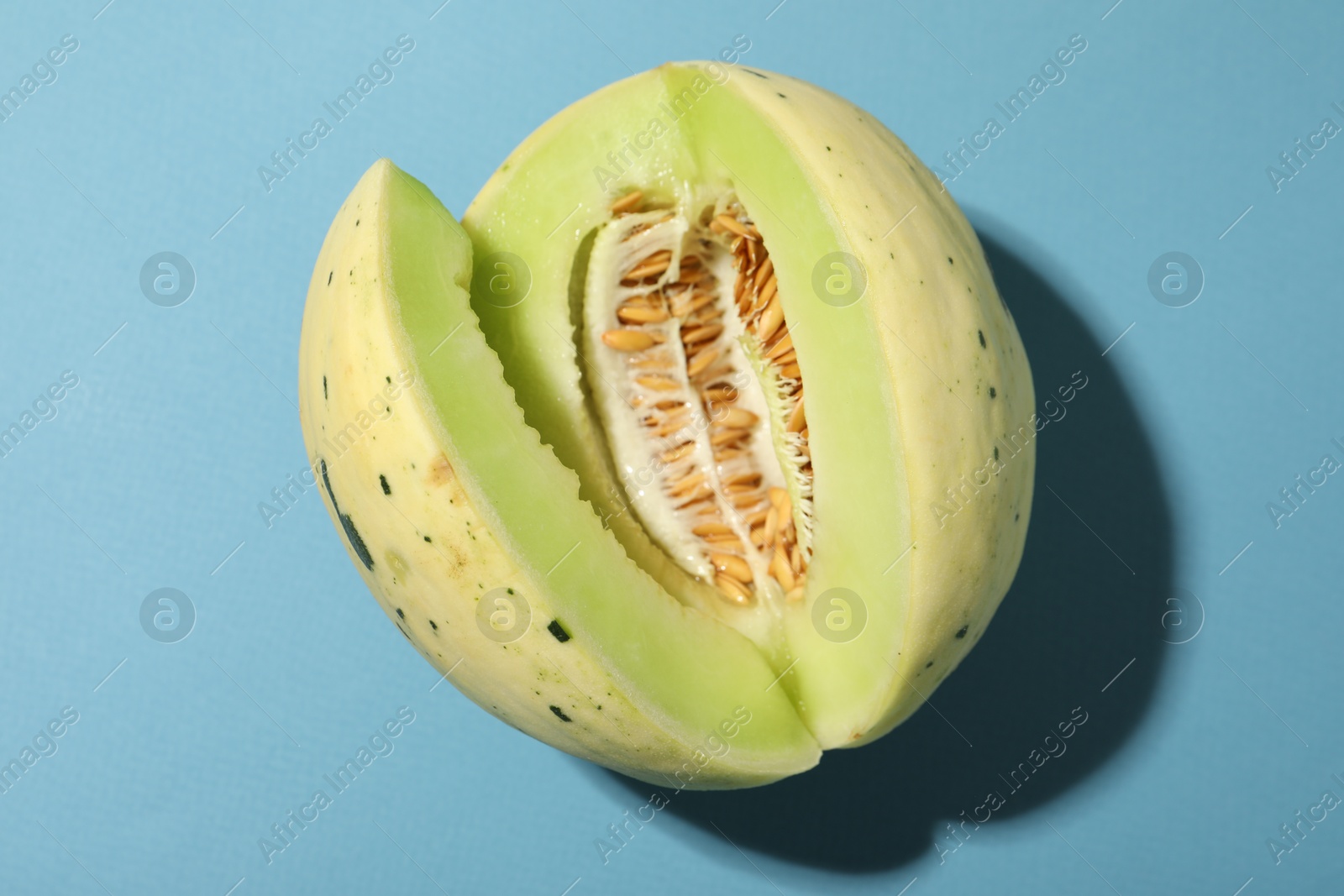 Photo of Cut fresh ripe honeydew melon on light blue background, top view