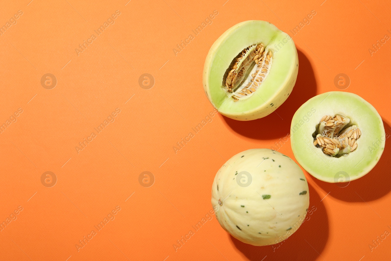 Photo of Fresh ripe honeydew melons on orange background, top view. Space for text