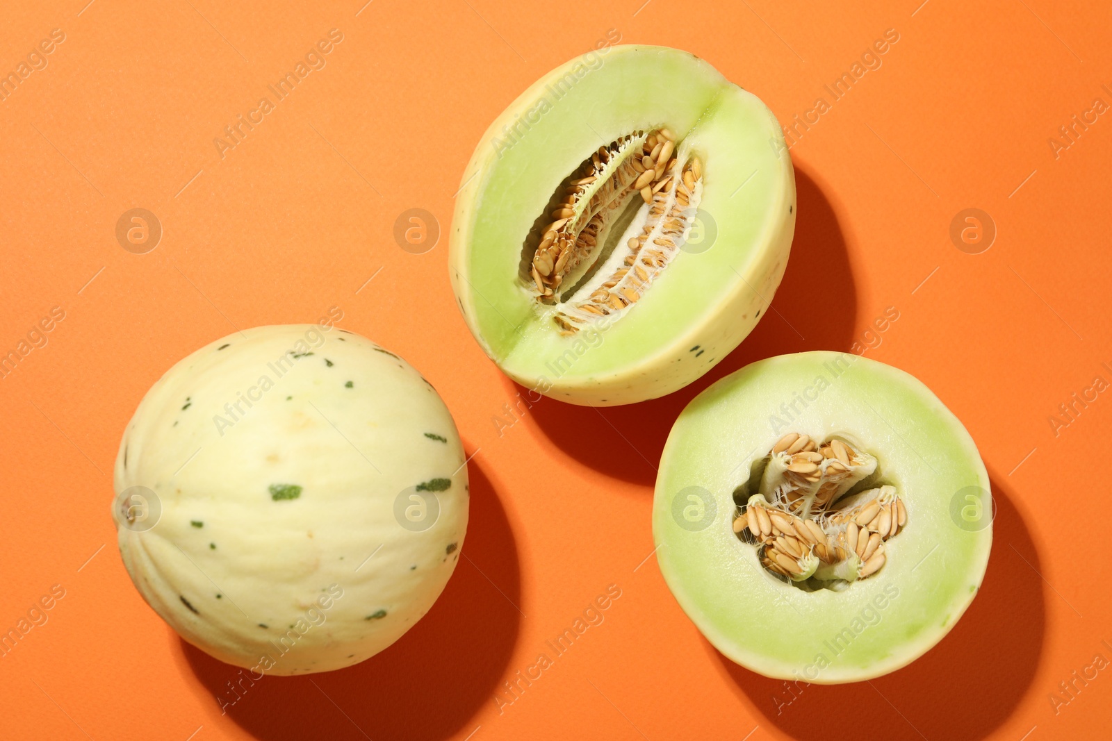 Photo of Fresh ripe honeydew melons on orange background, top view