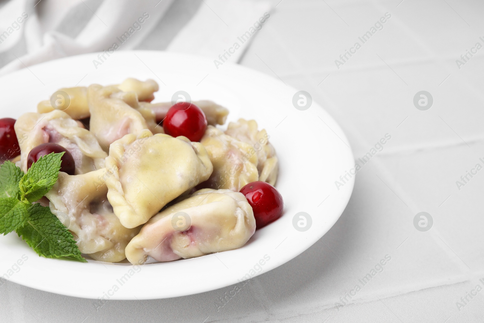 Photo of Traditional Ukrainian dumplings (varenyky) with cherries on white tiled table, closeup