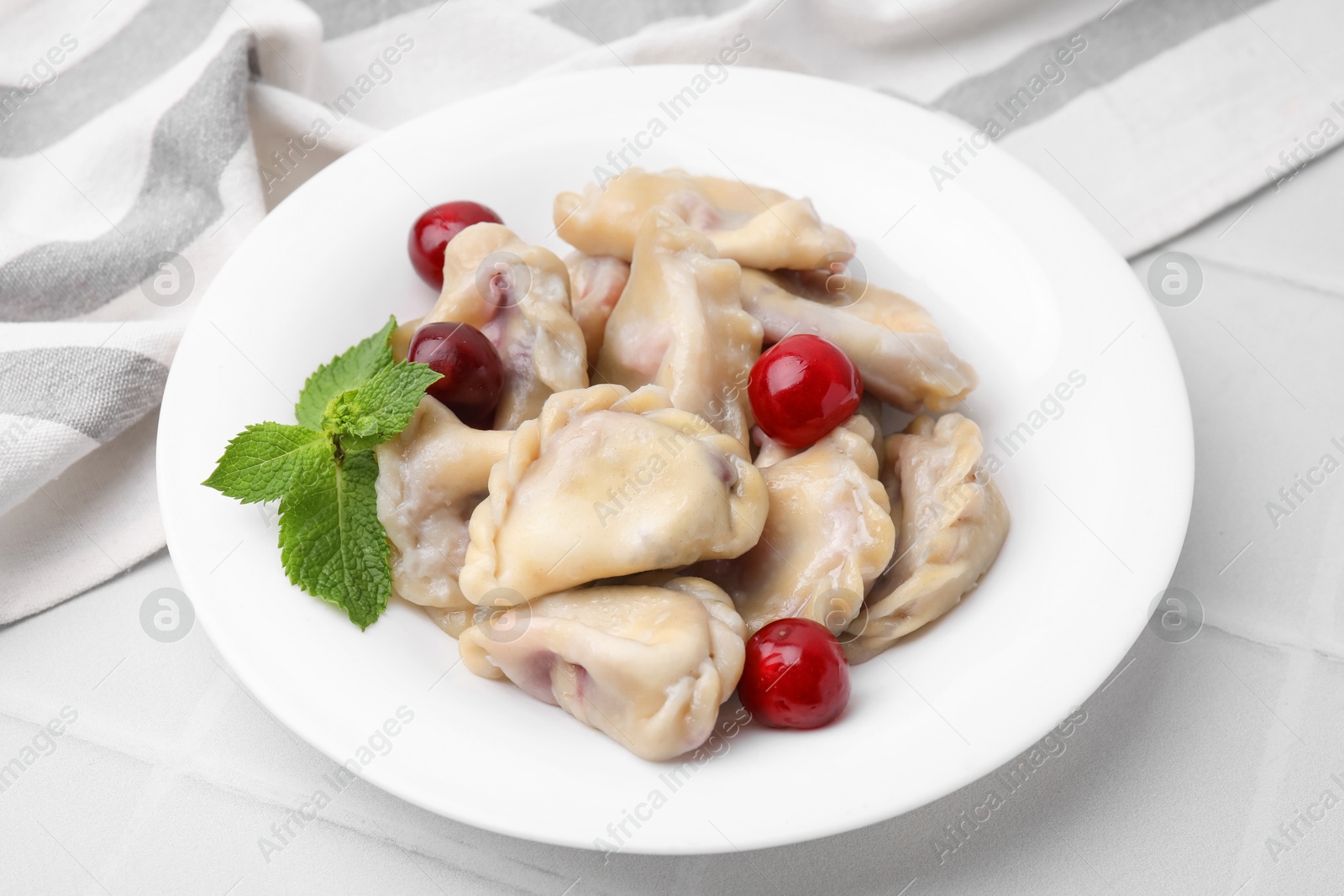 Photo of Traditional Ukrainian dumplings (varenyky) with cherries on white tiled table, closeup