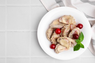 Photo of Traditional Ukrainian dumplings (varenyky) with cherries on white tiled table, top view