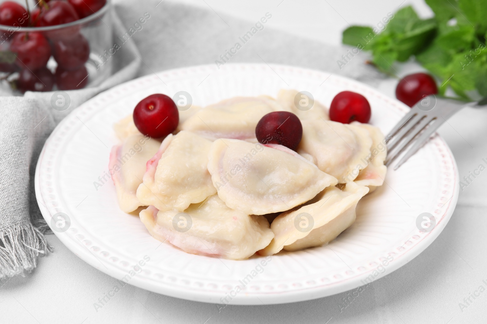 Photo of Traditional Ukrainian dumplings (varenyky) with cherries served on white tiled table, closeup