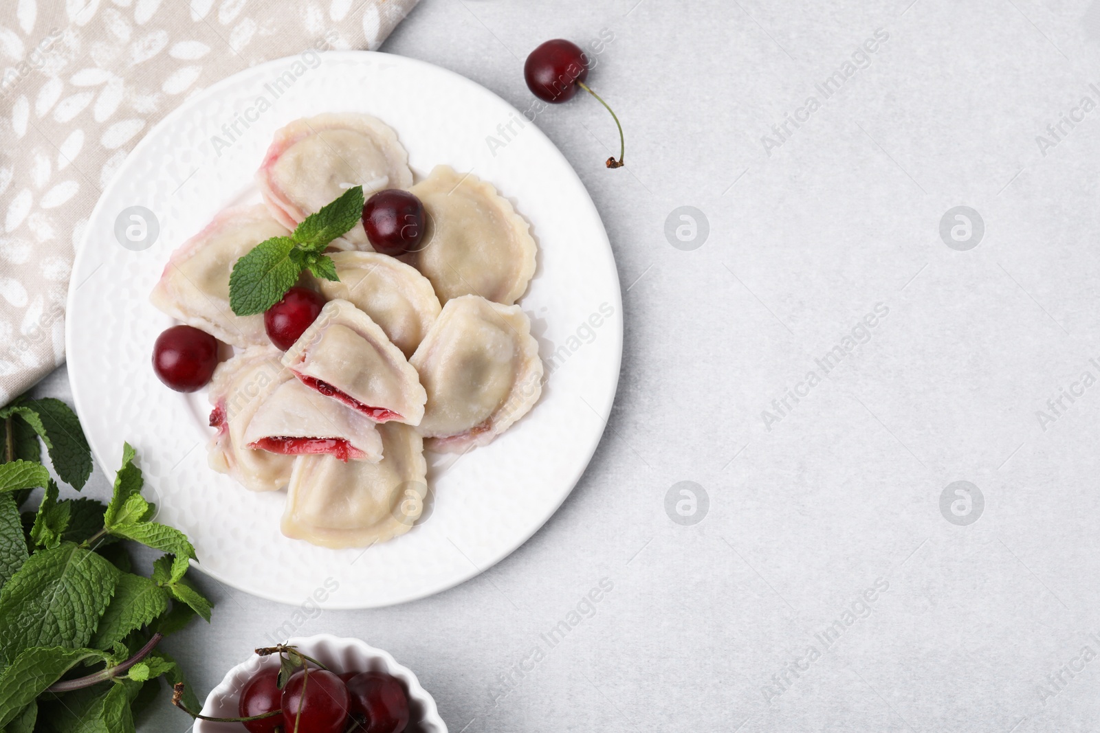 Photo of Traditional Ukrainian dumplings (varenyky) with cherries served on light table, flat lay. Space for text