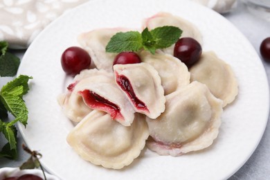 Photo of Traditional Ukrainian dumplings (varenyky) with cherries served on light table, closeup