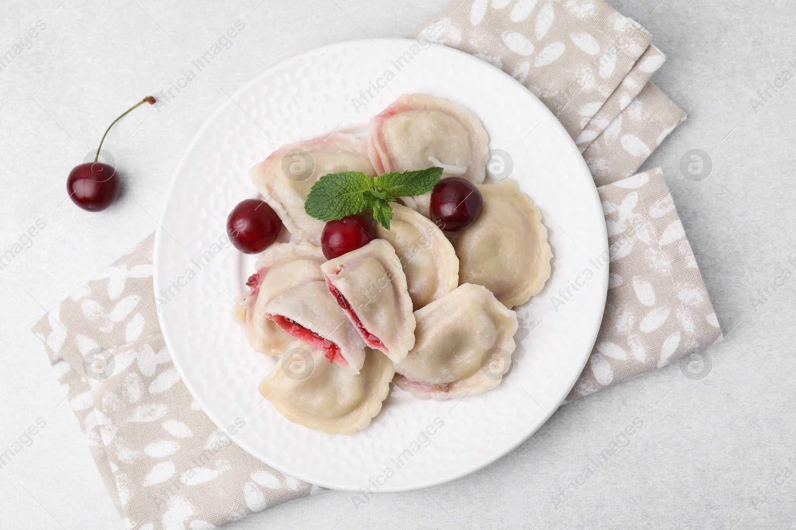 Photo of Traditional Ukrainian dumplings (varenyky) with cherries served on light table, flat lay