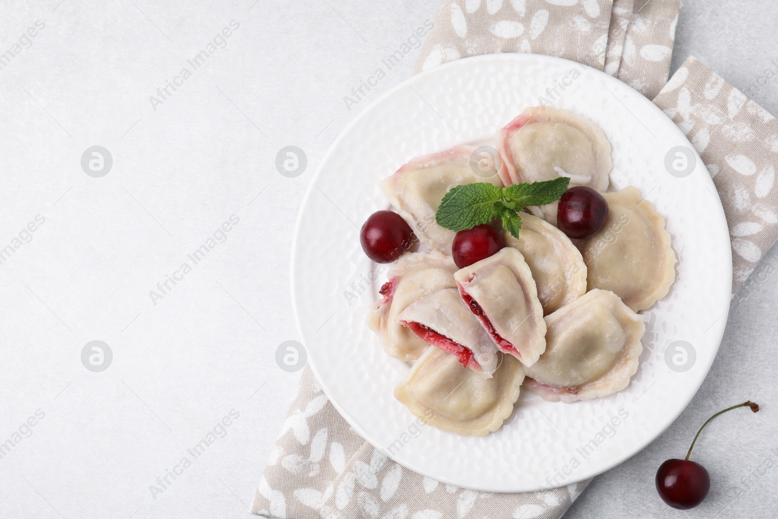 Photo of Traditional Ukrainian dumplings (varenyky) with cherries served on light table, flat lay. Space for text