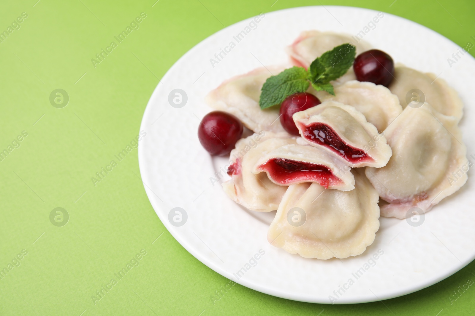 Photo of Traditional Ukrainian dumplings (varenyky) with cherries on green background, closeup. Space for text