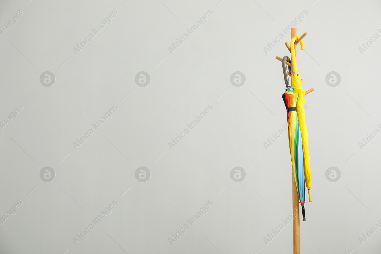 Photo of Colorful umbrellas on clothing rack against light grey background, space for text