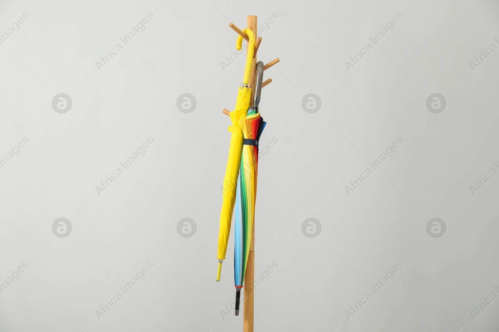 Photo of Colorful umbrellas on clothing rack against light grey background