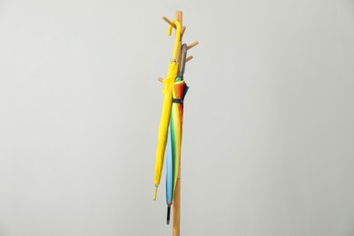 Photo of Colorful umbrellas on clothing rack against light grey background