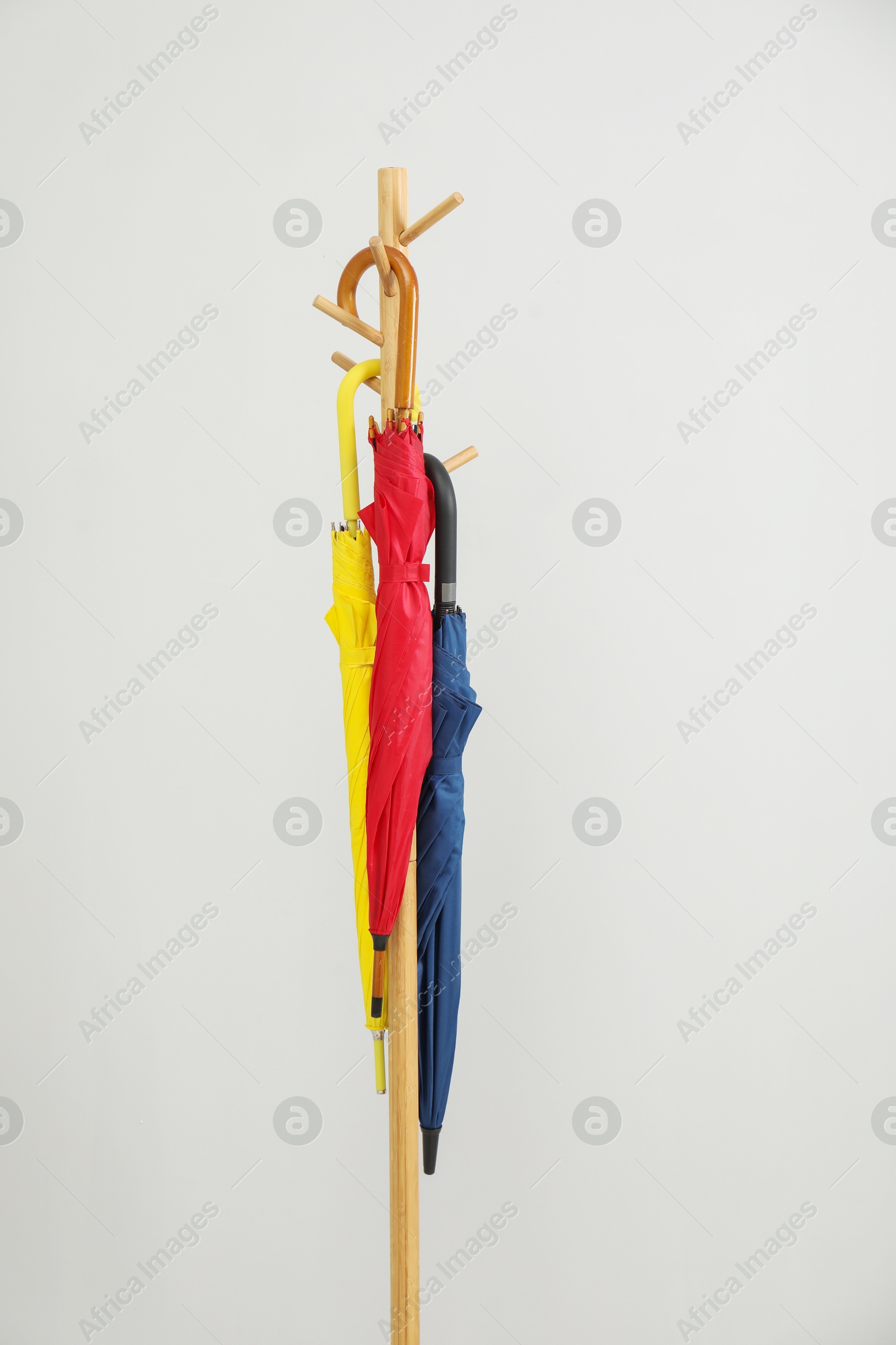 Photo of Colorful umbrellas on clothing rack against light grey background