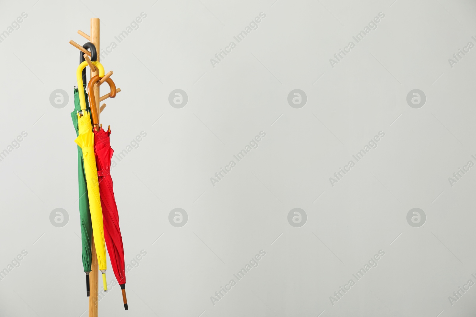 Photo of Colorful umbrellas on clothing rack against light grey background, space for text