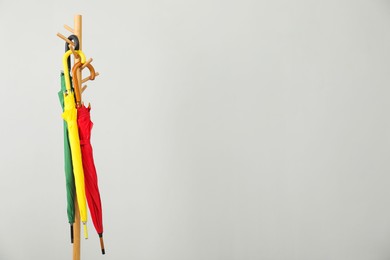 Colorful umbrellas on clothing rack against light grey background, space for text