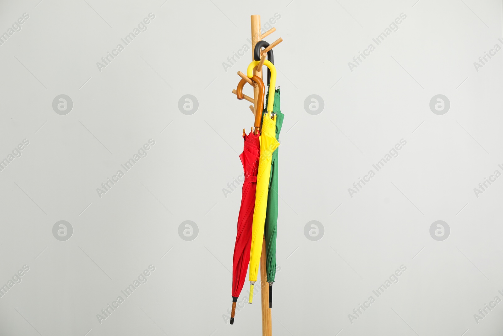 Photo of Colorful umbrellas on clothing rack against light grey background