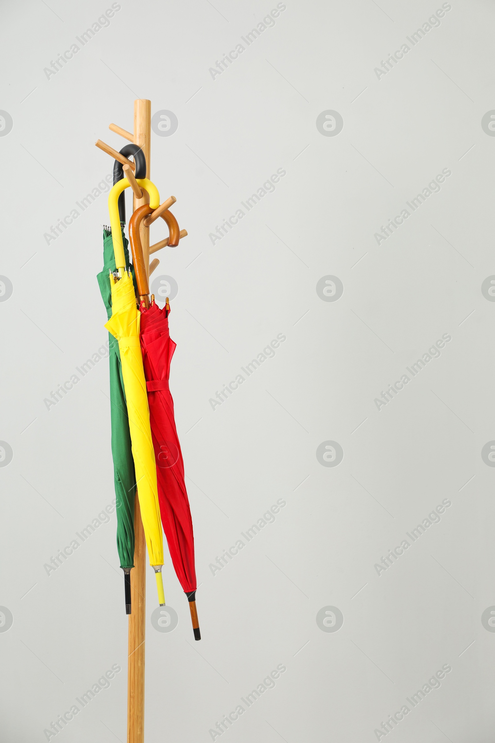 Photo of Colorful umbrellas on clothing rack against light grey background, space for text