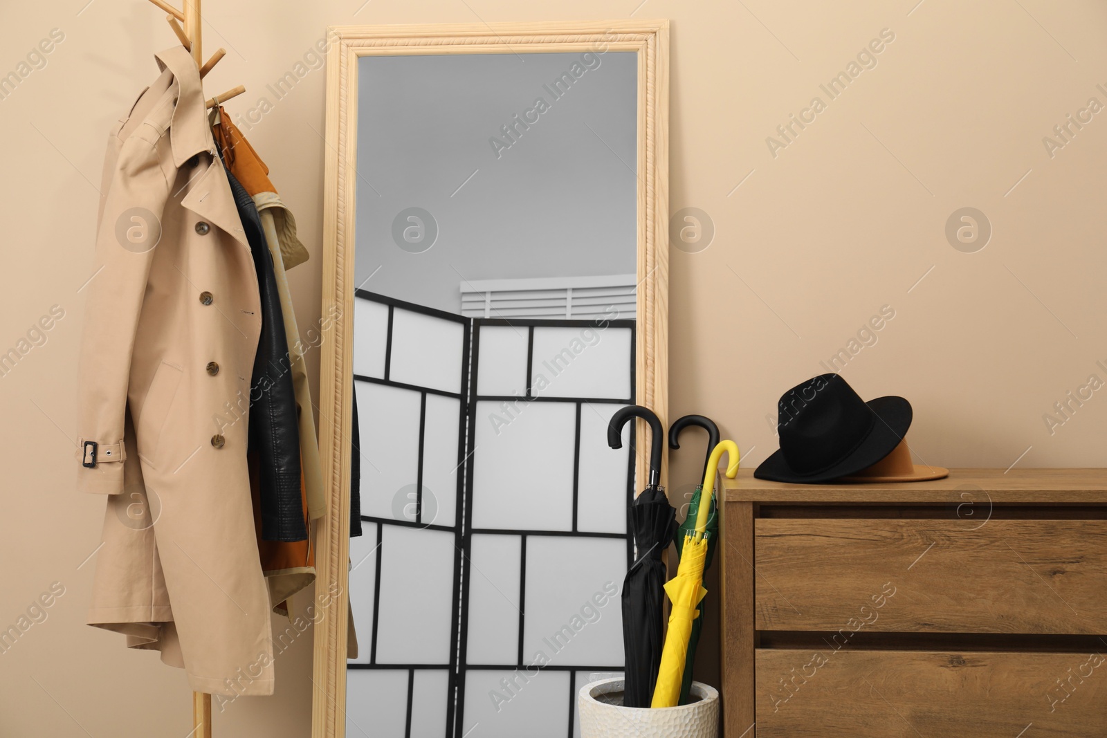 Photo of Colorful umbrellas in holder, rack with coat and jacket indoors