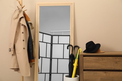 Colorful umbrellas in holder, rack with coat and jacket indoors