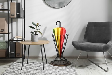 Photo of Colorful umbrella in stand, chair, coffee table and shelving unit indoors