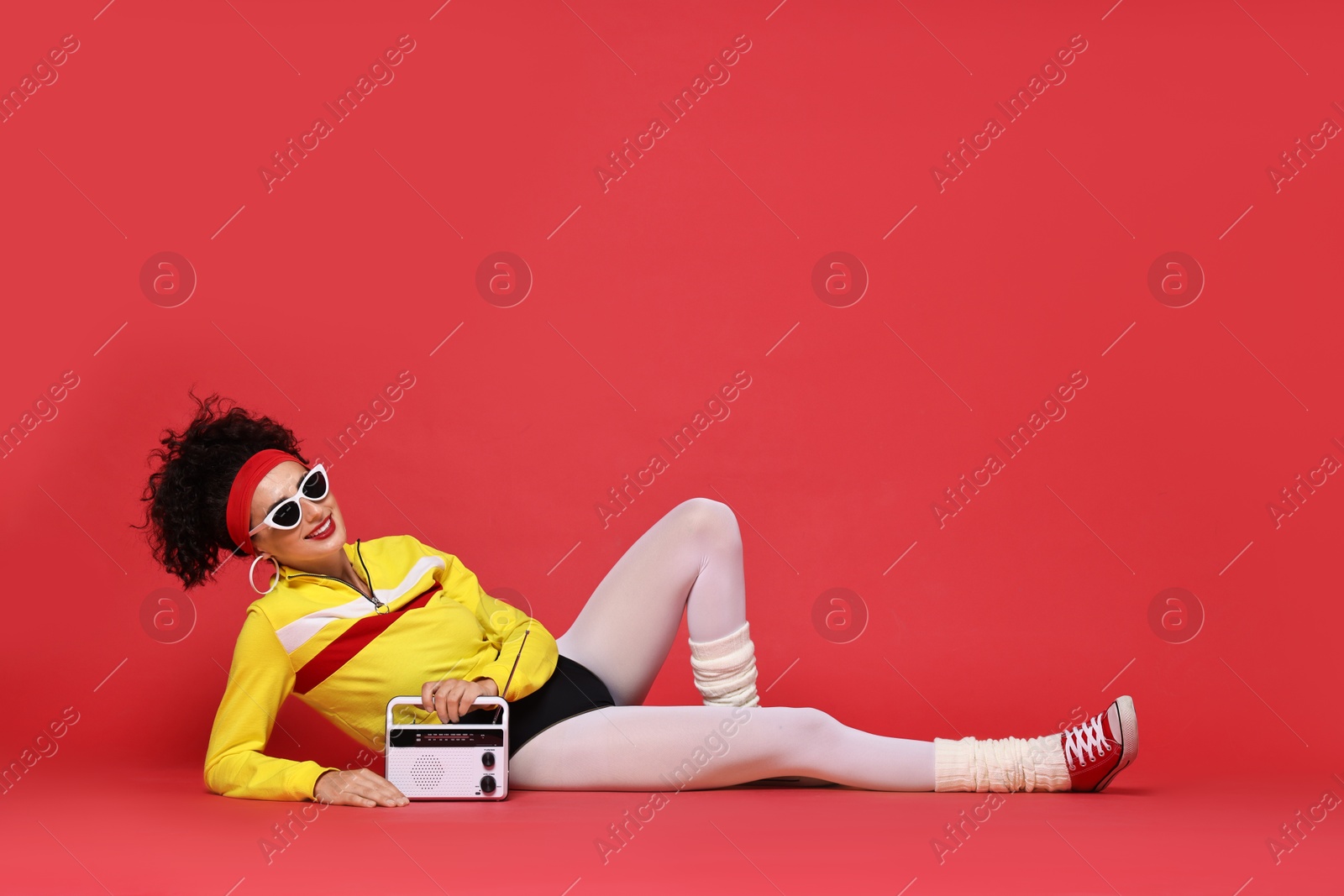 Photo of Aerobics. Woman in sportswear holding radio receiver on red background