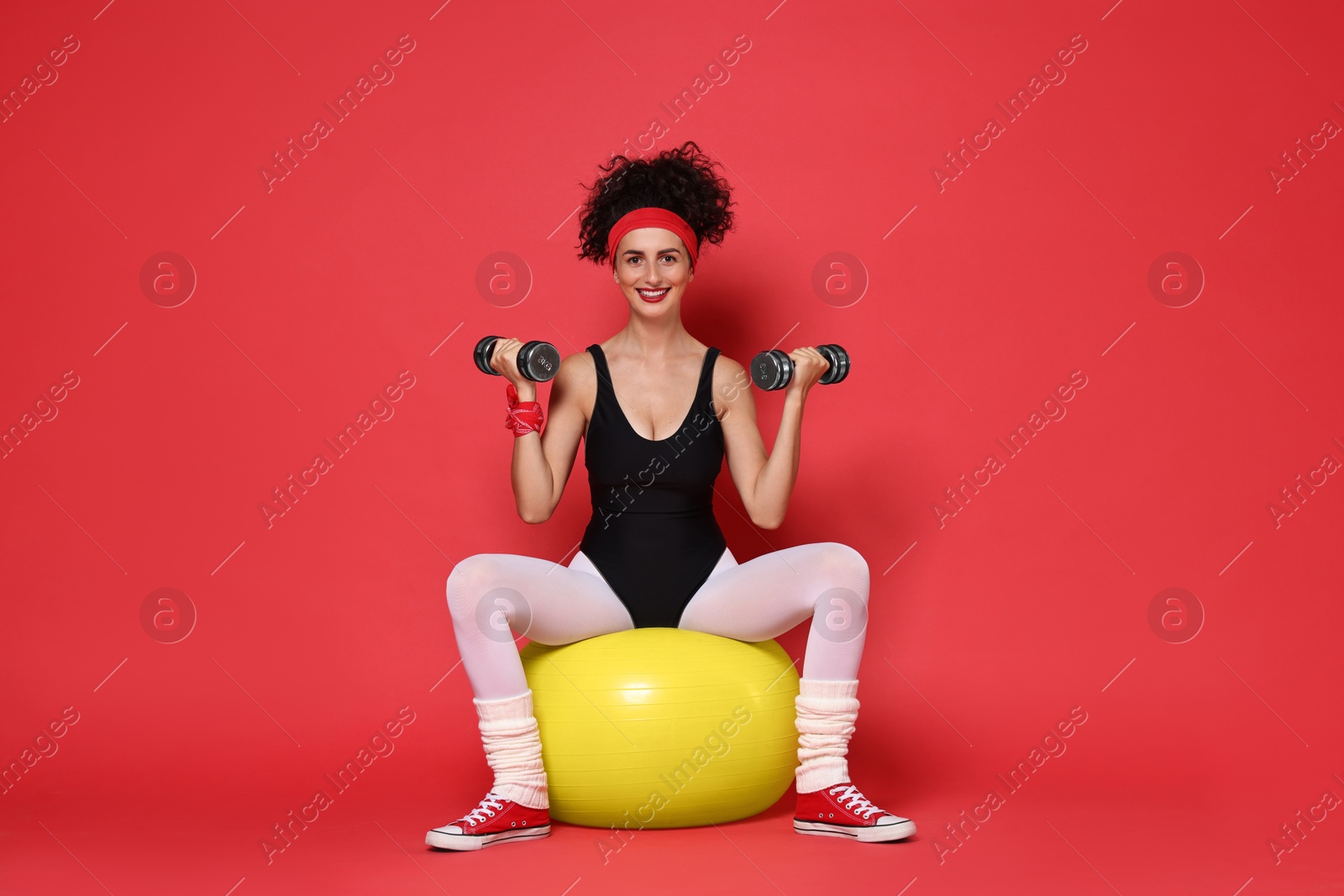 Photo of Woman doing aerobic exercise with dumbbells and fitness ball on red background