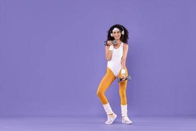 Woman in headphones doing aerobic exercise with dumbbells on purple background