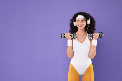 Woman in headphones doing aerobic exercise with dumbbells on purple background, space for text